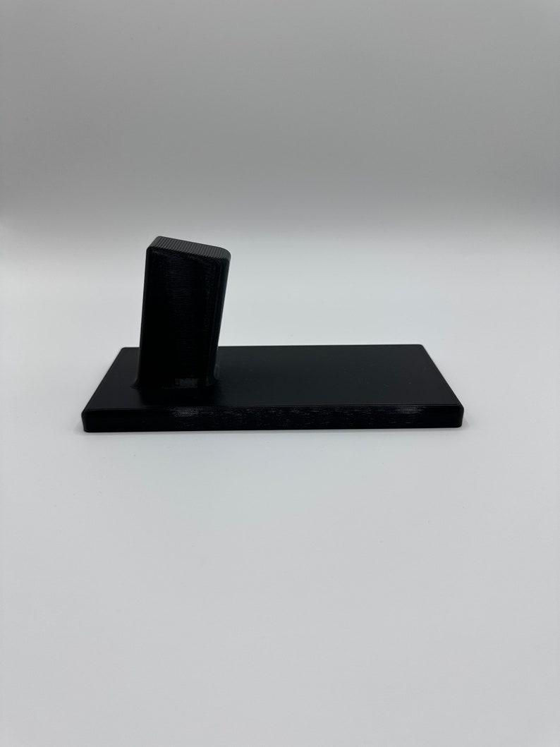 May include: A black plastic stand with a raised platform for displaying a small object.