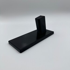 May include: A black plastic stand with a vertical slot for holding a phone or other device.