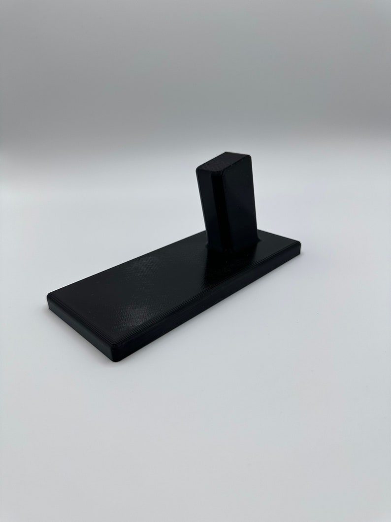 May include: A black plastic stand with a vertical slot for holding a phone or other device.