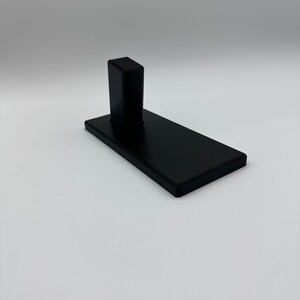 May include: A black plastic stand with a raised platform. The stand is designed to hold a small object, such as a phone or a tablet.