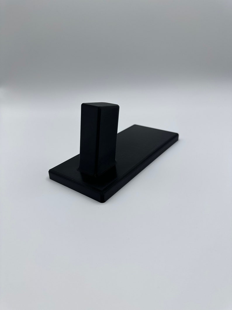 May include: A black wall-mounted hook with a rectangular base and a single vertical hook.