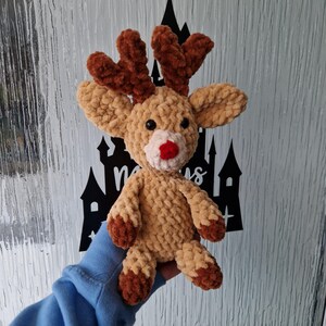 May include: A crocheted reindeer plush toy with brown antlers and a red nose. The reindeer is light brown and has a fuzzy texture.
