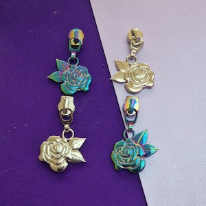May include: Two sets of zipper pulls with rose charms. One set has iridescent rose charms and zipper pulls, the other set has gold-toned rose charms and zipper pulls. The background is purple and light purple.