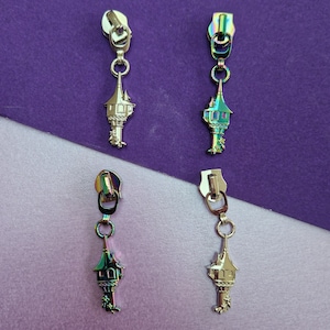 May include: Four iridescent silver zipper pulls shaped like a tower with a pointed roof. Each pull has a small loop at the top and a decorative design on the tower.