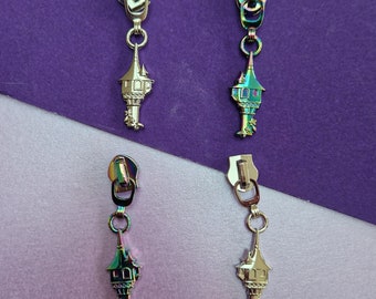 May include: Four iridescent silver zipper pulls shaped like a tower with a pointed roof. Each pull has a small loop at the top and a decorative design on the tower.