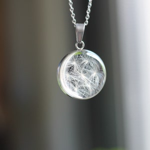 Peut inclure: Un collier en argent avec un pendentif rond représentant une tête de pissenlit blanche enrobée de résine transparente.
