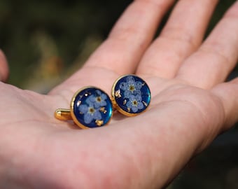May include: A pair of gold cufflinks with blue resin and pressed forget-me-not flowers.