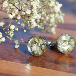 May include: A pair of silver cufflinks with small white flowers encased in clear resin.