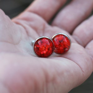 Può includere: Un paio di gemelli d'argento con fiori rossi pressati incapsulati in resina trasparente.