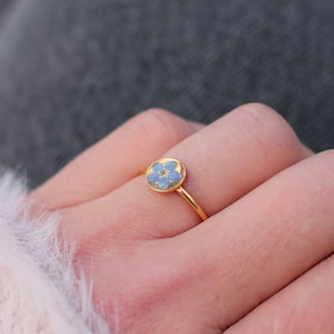 Puede incluir: Un anillo de oro con una flor de nomeolvides azul encapsulada en resina.