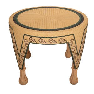 May include: A round, woven wicker side table with a light brown finish. The table features a dark green border and decorative trim with geometric patterns. The legs are carved and have a light brown finish.
