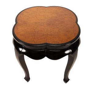 May include: A small, decorative table with a unique clover-shaped top. The tabletop features a warm, brown wood grain pattern, framed by a black border. The base and legs are glossy black, with curved legs for a classic look.