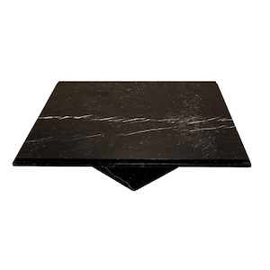 May include: A square, black marble table top with white veining. The table top is supported by a triangular base. The design is modern and minimalist, suitable for various interior styles.