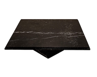 May include: A square, black marble table top with white veining. The table top is supported by a triangular base. The design is modern and minimalist, suitable for various interior styles.
