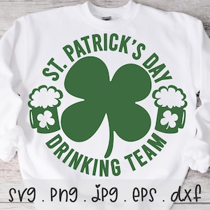 Może przedstawiać: Biała bluza z zieloną koniczyną i tekstem "St. Patrick's Day Drinking Team" w kółku. Wzór zawiera również dwa zielone kufle piwa z białą pianą.