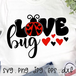 Op de afbeelding: Een wit T-shirt met een zwart en rood ontwerp met de tekst "Love Bug" en een lieveheersbeestje-afbeelding. Het lieveheersbeestje is rood met zwarte stippen en heeft zwarte vleugels. Het woord "Love" staat in grote zwarte letters en het woord "Bug" staat in een cursief schrift.