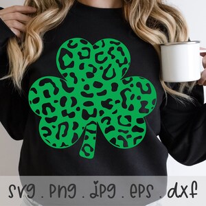 Può includere: Una felpa nera con un design a trifoglio verde. Il trifoglio è composto da un motivo a stampa leopardata.