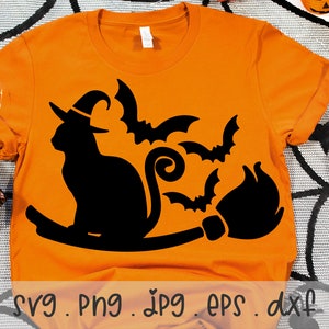Puede incluir: Camiseta naranja con una silueta negra de un gato con un sombrero de bruja y montando una escoba con murciélagos volando a su alrededor.