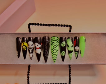 Puede incluir: Un conjunto de diez uñas postizas de Halloween de color negro y verde con varios diseños, incluyendo una espiral, dados y un personaje de Pesadilla antes de Navidad.