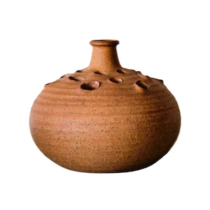 Może przedstawiać: Terakotowy brązowy ceramiczny wazon o okrągłym korpusie i krótkiej szyjce. Wazon ma wiele małych otworów wokół górnej części, aby trzymać kwiaty.