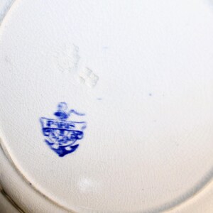 May include: Close-up of the bottom of a white ceramic plate with a blue anchor and the text "FINE CHINA" in a shield.