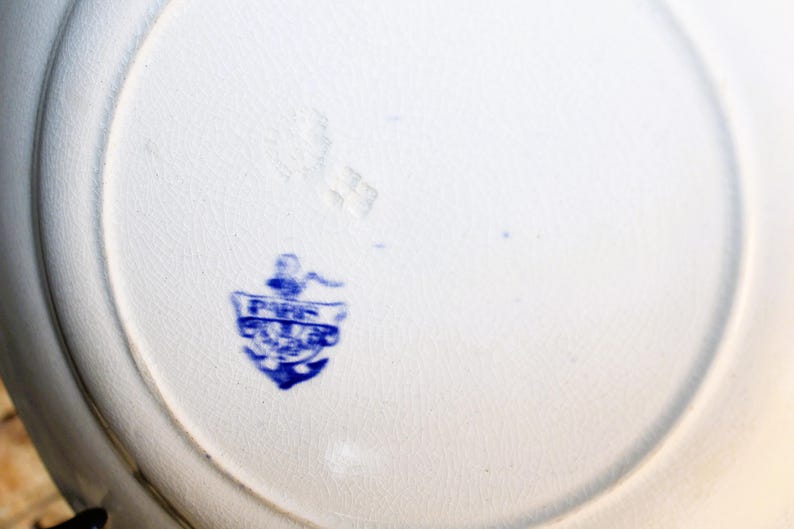 May include: Close-up of the bottom of a white ceramic plate with a blue anchor and the text "FINE CHINA" in a shield.