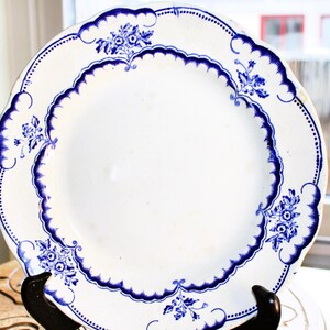 May include: A white ceramic plate with a blue floral design. The plate has a scalloped edge and a raised rim.