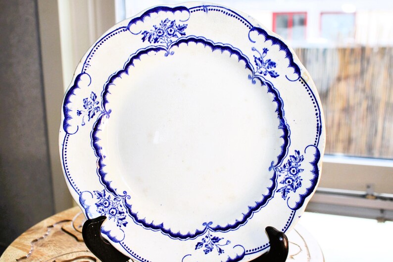 May include: A white ceramic plate with a blue floral design. The plate has a scalloped edge and a raised rim.