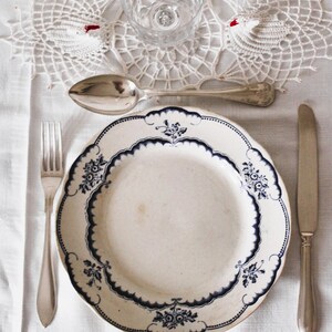 May include: A white porcelain dinner plate with a blue and white floral pattern. The plate is set on a white tablecloth with a silver fork, spoon, and knife.