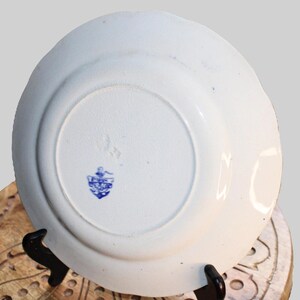 May include: A white ceramic plate with a blue and white floral design. The back of the plate has a blue and white logo with the text "The Anchor" in a shield.