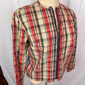 May include: A long-sleeved jacket featuring a plaid pattern in red, navy blue, and cream. The garment has a round neckline and a full-length front zipper closure with a circular metal pull tab. The fabric has a visible woven texture throughout.
