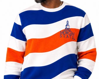 May include: A long-sleeve crewneck sweatshirt featuring wide, diagonal stripes in white, royal blue, and bright orange. The chest displays an embroidered graphic of a building cupola above the text MORGAN STATE in blue lettering.