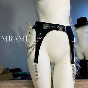 May include: Black leather garter belt with silver chain accents. The belt has a buckle closure and is designed to be worn around the waist.