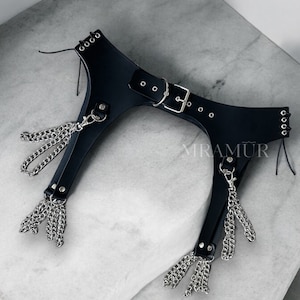 May include: Black leather garter belt with silver chain tassels. The belt has a buckle closure and multiple rows of eyelets. The text "MRAMUR" is visible on the belt.