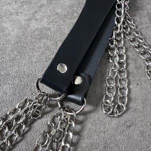 May include: A black leather strap with three silver chains attached. The strap has two silver metal rivets.