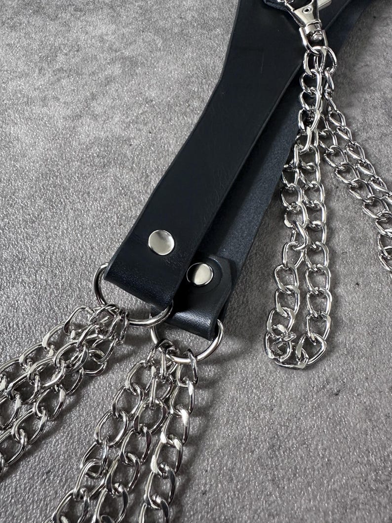 May include: A black leather strap with three silver chains attached. The strap has two silver metal rivets.