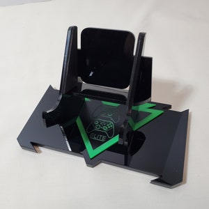 May include: Black acrylic stand with a green triangle design featuring a video game controller graphic and the word "ELITE". The stand is designed to hold a video game controller.