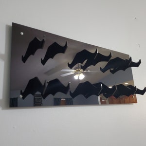 Pode incluir: Um espelho preto com um design decorativo de v&aacute;rios bigodes pretos presos &agrave; superf&iacute;cie. O espelho est&aacute; montado em uma parede branca.