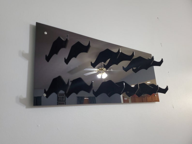 Pode incluir: Um espelho preto com um design decorativo de v&aacute;rios bigodes pretos presos &agrave; superf&iacute;cie. O espelho est&aacute; montado em uma parede branca.