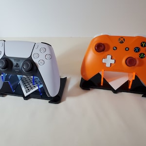 May include: A black stand with two video game controllers. One controller is white and the other is orange.
