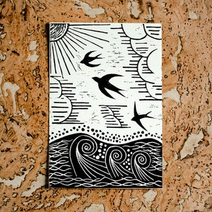 May include: Black and white linocut print of a sun, clouds, birds, and waves. The print is on a white background and has a rustic, handmade feel.