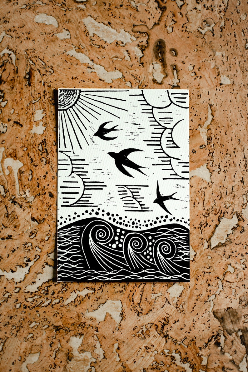 May include: Black and white linocut print of a sun, clouds, birds, and waves. The print is on a white background and has a rustic, handmade feel.