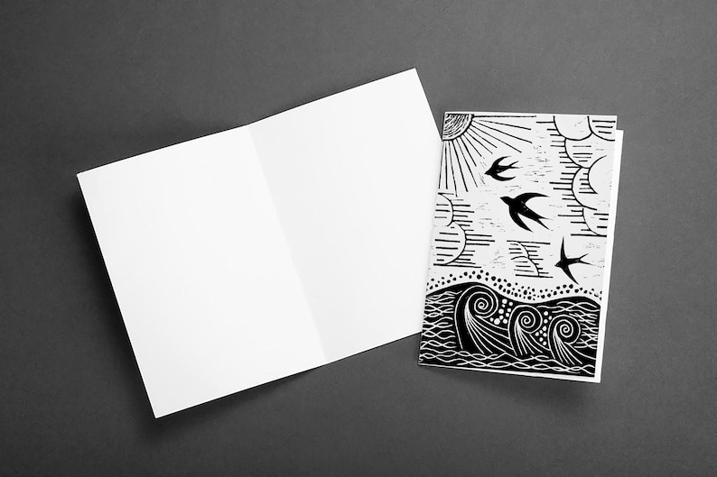 May include: A blank white card with a folded edge is next to a card with a black and white illustration of a sun, clouds, birds, and waves.