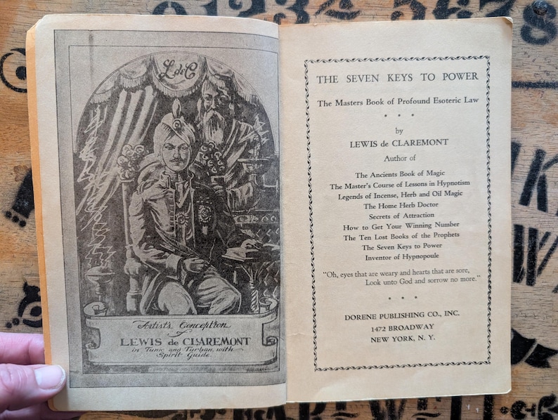 May include: An open book titled The Seven Keys to Power by Lewis de Claremont. The left page features a black and white illustration of a person in a turban and tunic with a spirit guide. The right page lists the author's other book titles.