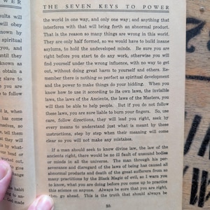 May include: An open book page titled The Seven Keys to Power with black printed text on off-white paper. The page contains paragraphs discussing spiritual development, divine law, and the laws of the Ancients, with the page number 35 at the bottom.