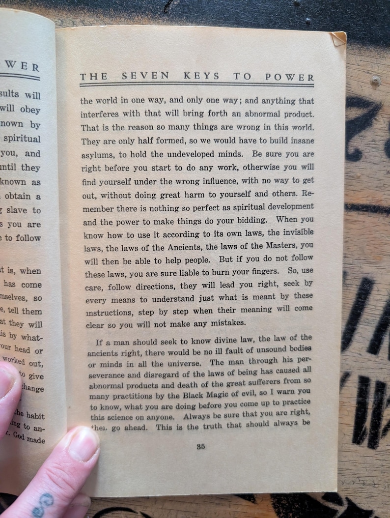 May include: An open book page titled The Seven Keys to Power with black printed text on off-white paper. The page contains paragraphs discussing spiritual development, divine law, and the laws of the Ancients, with the page number 35 at the bottom.