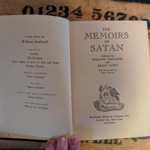 May include: Open book with the title "The Memoirs of Satan" on the right page. The left page lists other books by William Gerhardi. The book has a decorative illustration and is published by Doubleday, Doran & Company, Inc.
