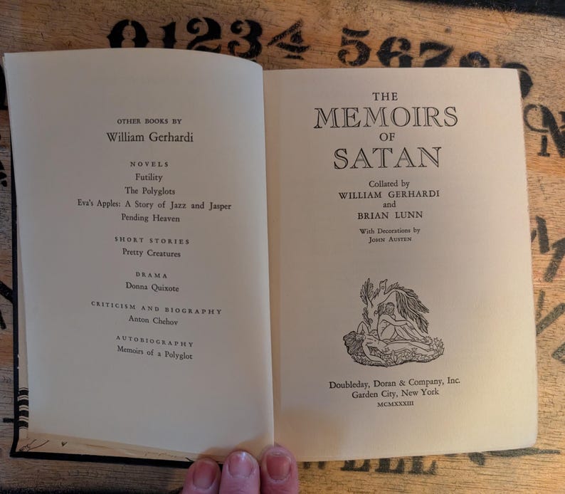 May include: Open book with the title "The Memoirs of Satan" on the right page. The left page lists other books by William Gerhardi. The book has a decorative illustration and is published by Doubleday, Doran & Company, Inc.