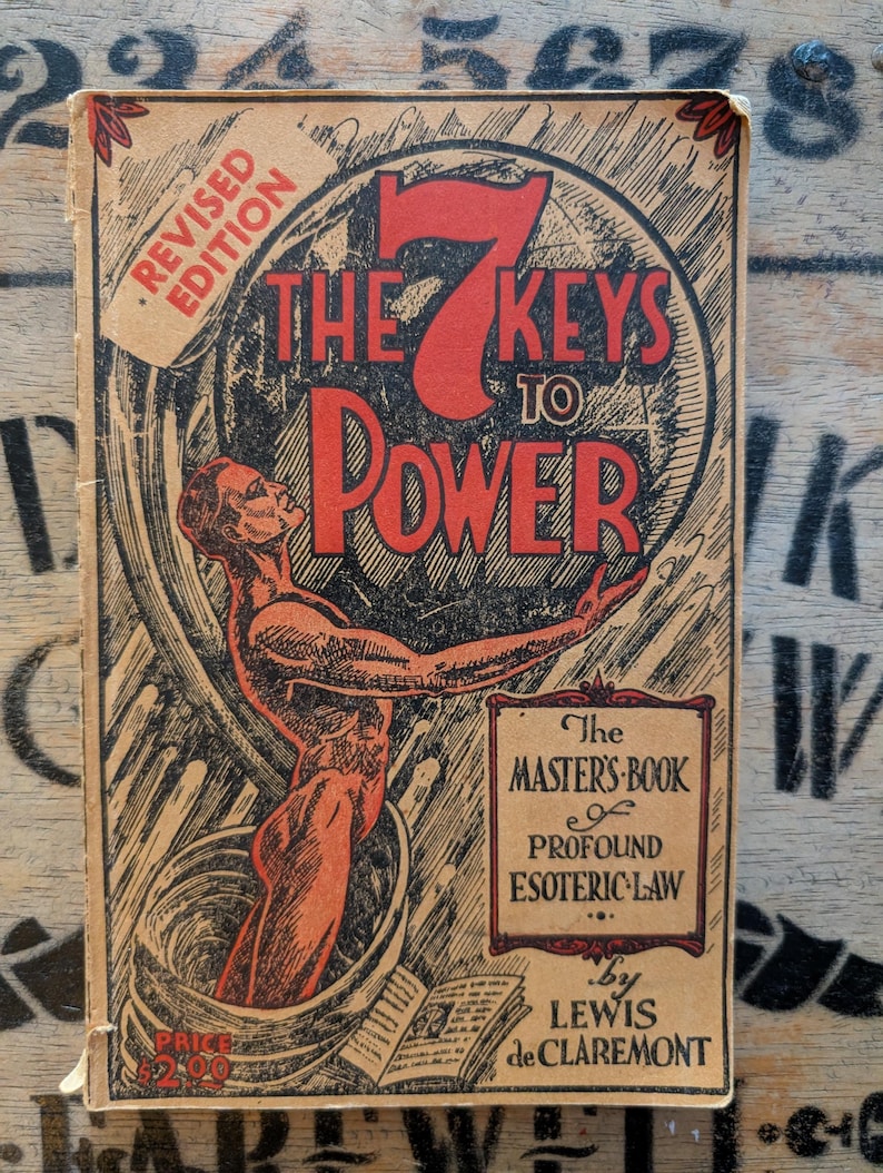 May include: A vintage book titled The 7 Keys to Power by Lewis de Claremont. The cover features a red illustration of a figure emerging from a vessel, with the text Revised Edition, The Master's Book of Profound Esoteric Law, and Price $2.00.