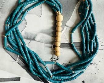May include: A multi-strand necklace made of teal blue and light blue wooden beads. The necklace is layered and has a long strand of natural wood beads.